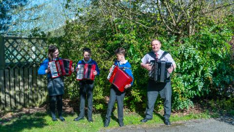 Three pupils in the garden learning to play the accordion with their tutor