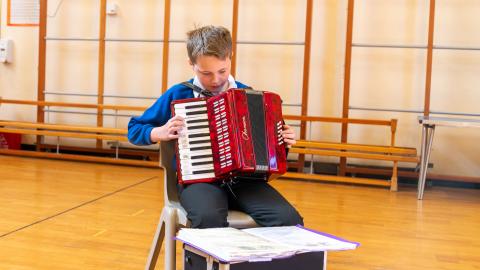 Boy in the hall reading music and playing the accordion 