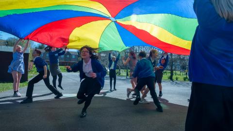 Pupils running about whilst others hold a parachute over their  heads