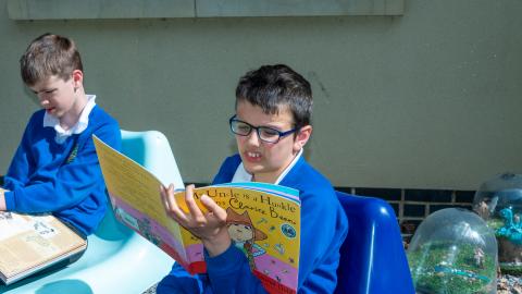 Boy sat outside in the sunshine reading a book